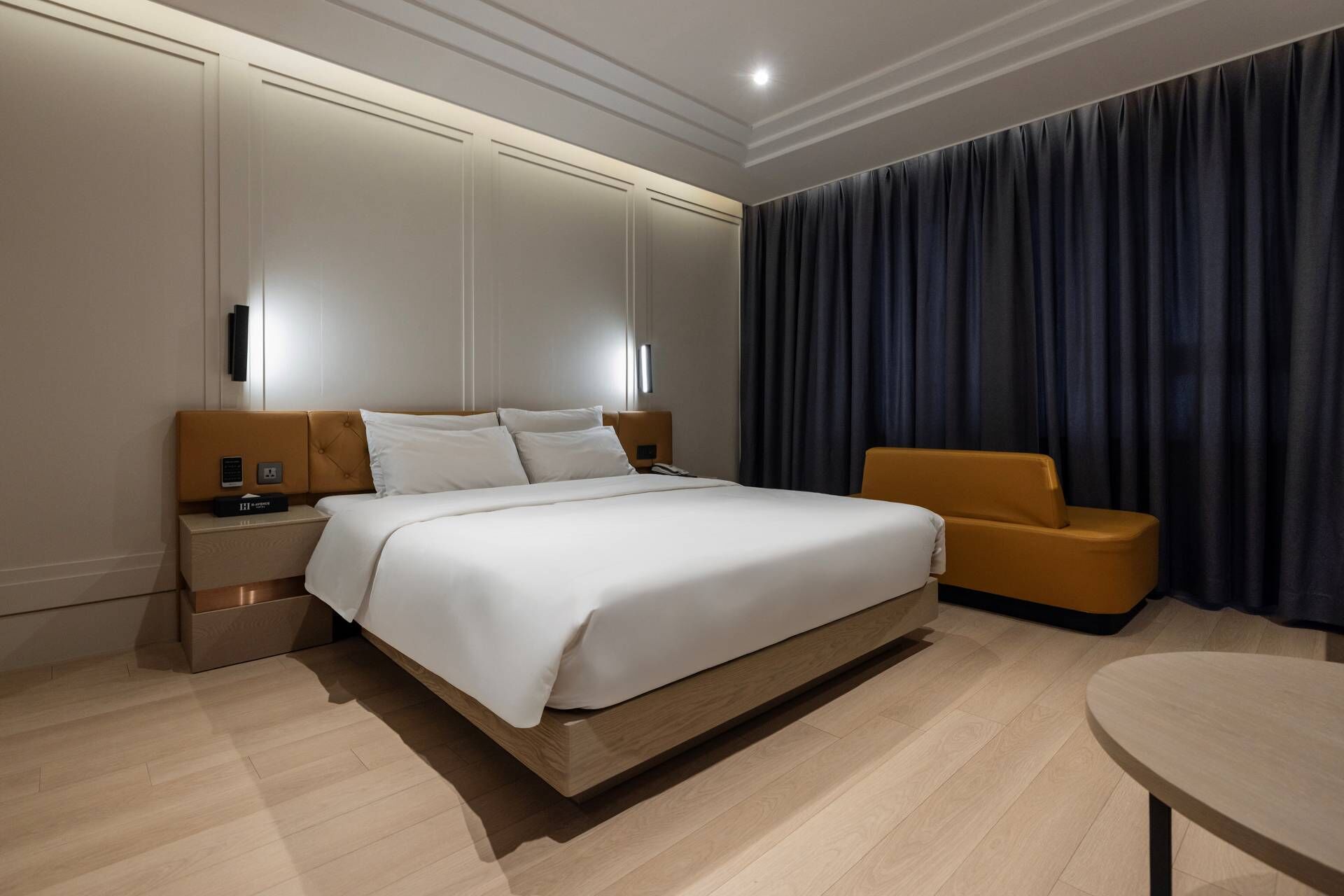 A modern hotel room with a large bed, bedside tables, a small table, and a dark curtain.
