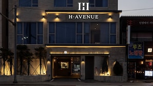 Un hôtel appelé H. Avenue, qui se distingue par son entrée imposante et un panneau indiquant la présence d’un parking.