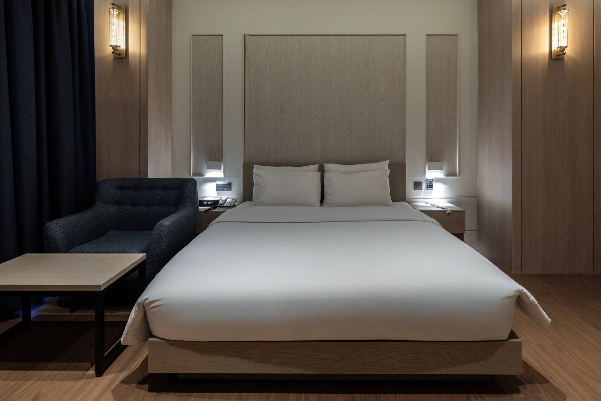 Moderni hotellihuone, jossa on suuri sänky, pieni työpöytä, tuoli sekä kaksi yöpöytää, joissa on lamput.