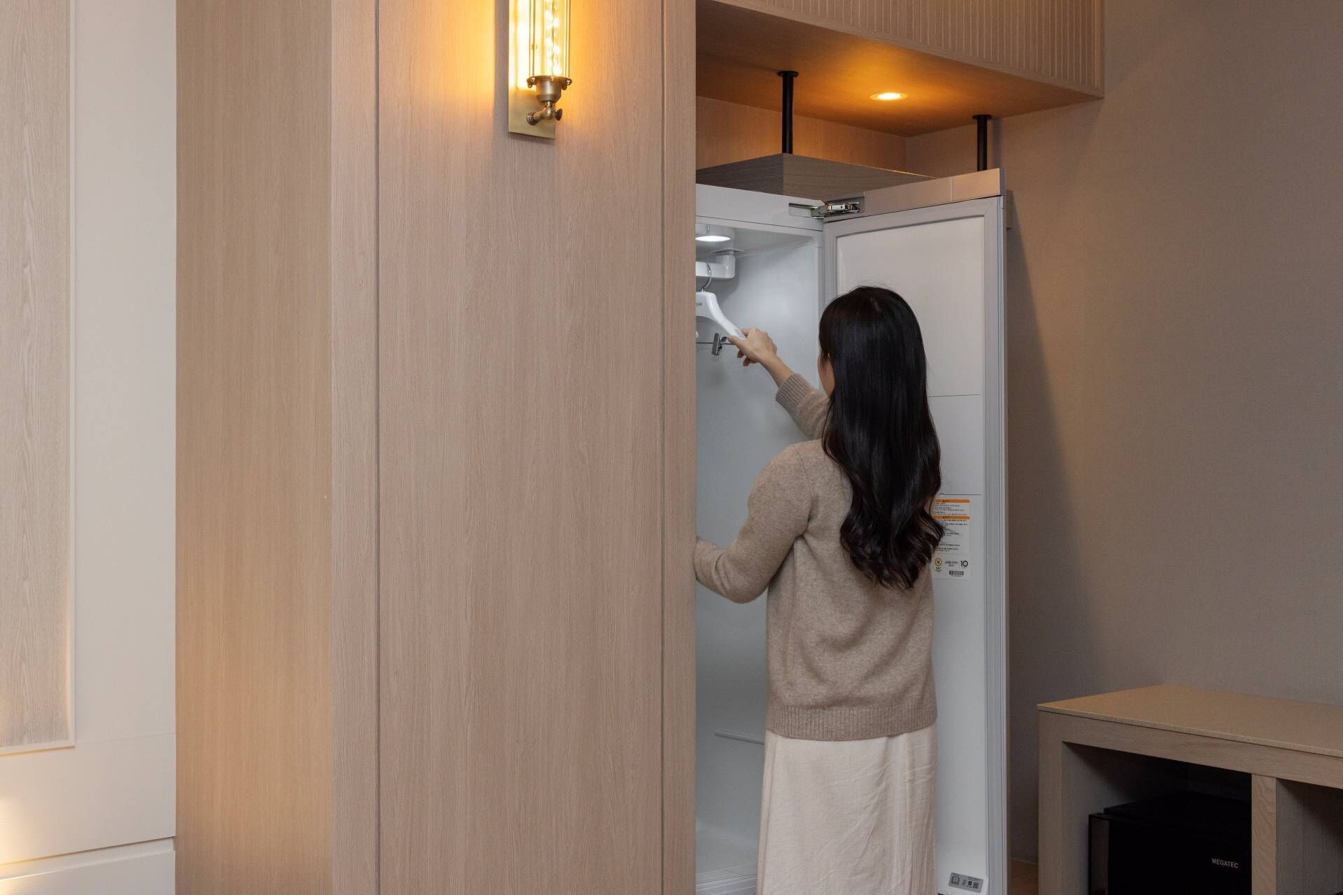 Une personne est en train d’installer une douche murale blanche dans une pièce dont les murs sont recouverts de lambris en bois et qui est éclairée par un luminaire au plafond.