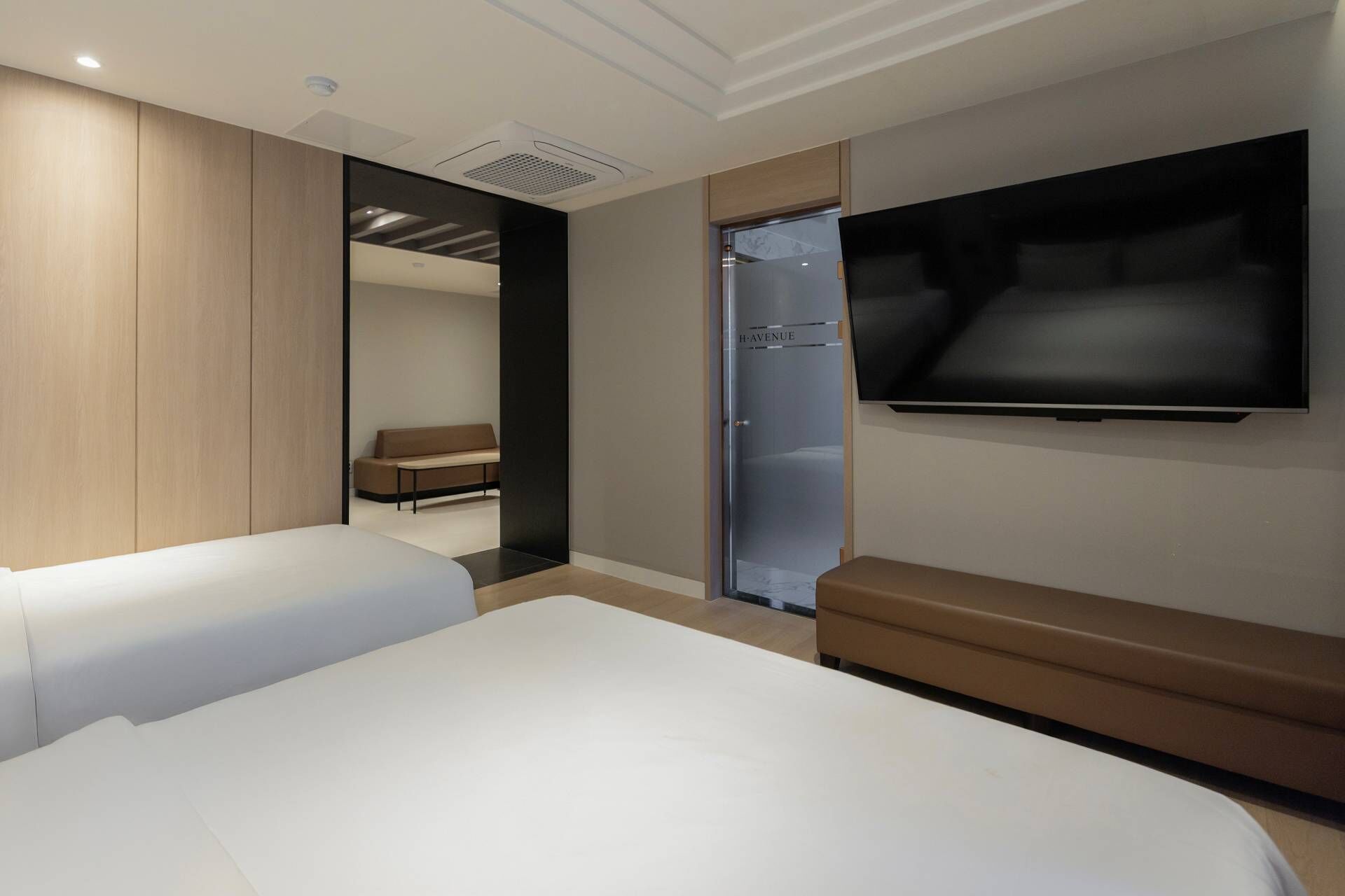 A modern hotel room with a large bed, a bench, a shower, and a TV mounted on the wall.