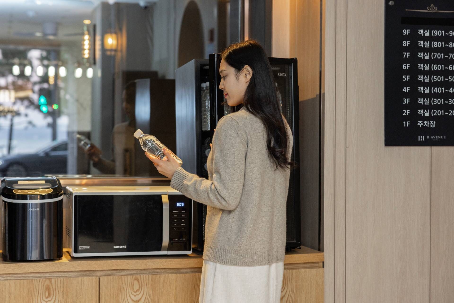 A person holding a water bottle in front of a microwave and a refrigerator.