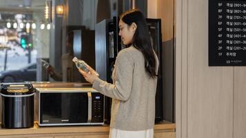 A person holding a water bottle in front of a microwave and a refrigerator.