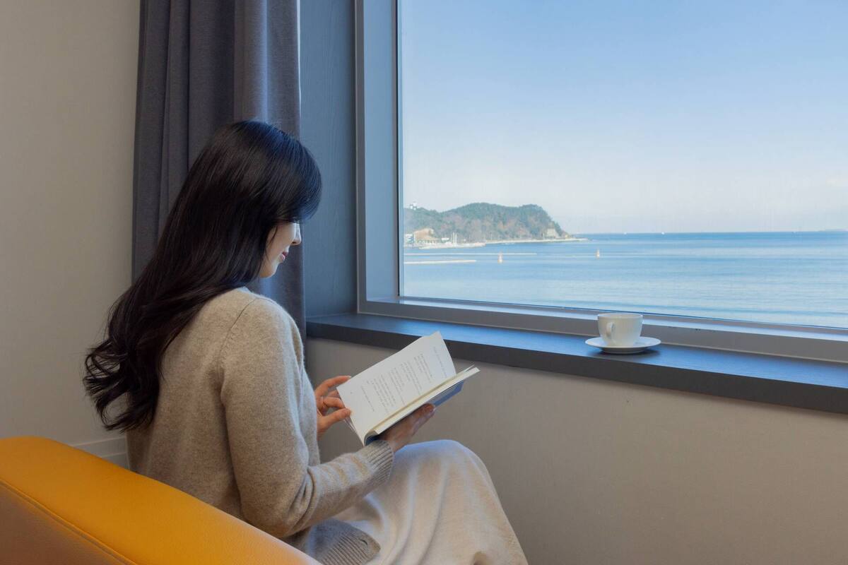 Une personne assise près d’une fenêtre, avec vue sur la mer.