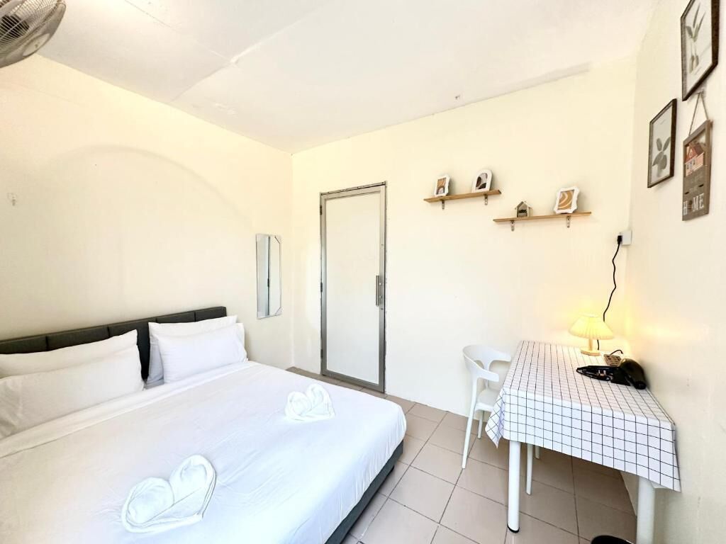 A hotel room with a bed, a desk with a lamp, a chair, and a door.