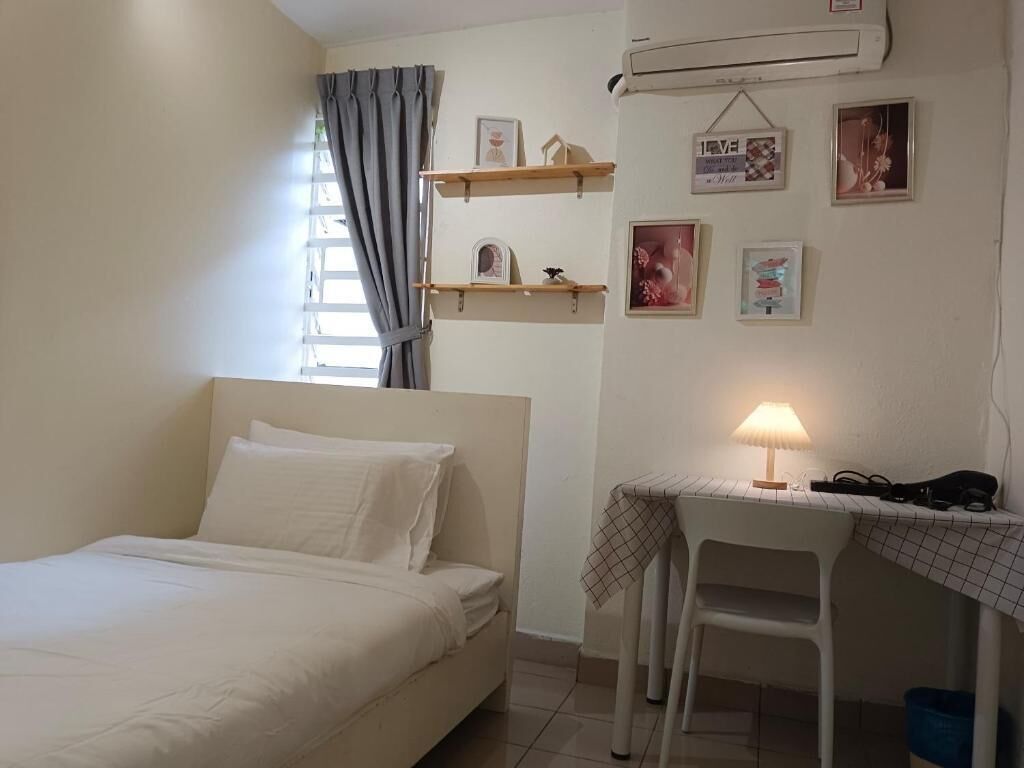 A bedroom with a bed, a desk with a lamp, and wall-mounted shelves with pictures.