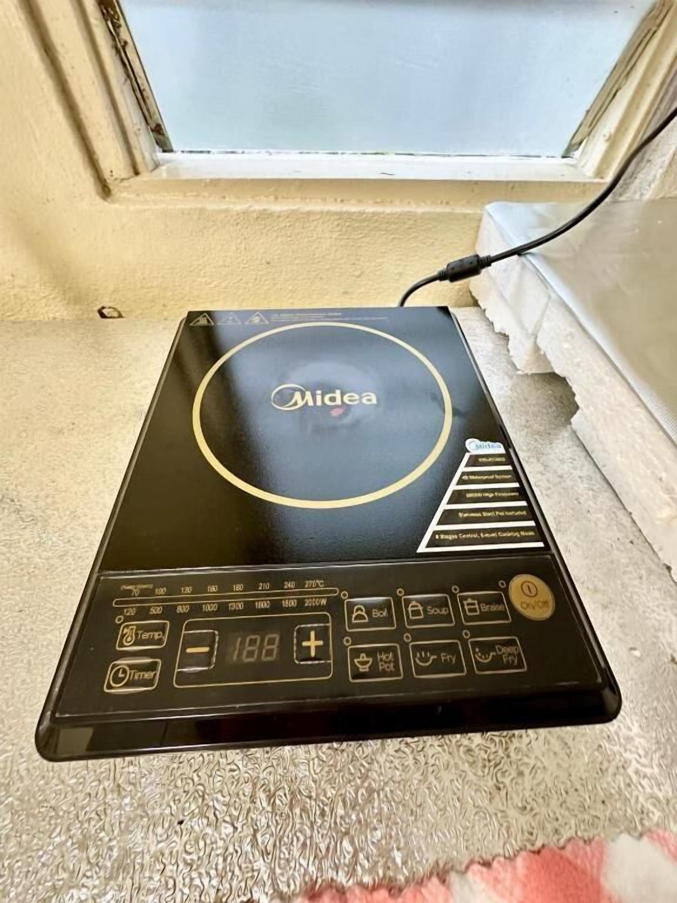 A black Midea induction cooktop with a digital display, buttons for various cooking functions, and a power cord plugged in.