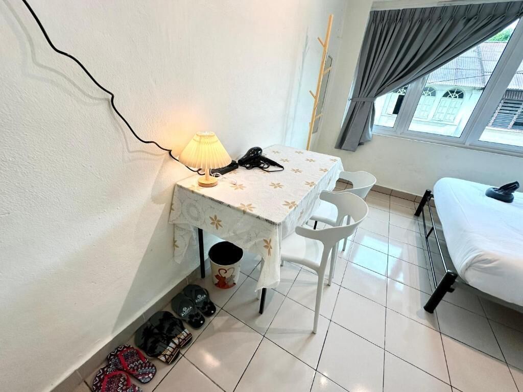 A small room with a bed, a table with a lamp, a chair, and a window with curtains.