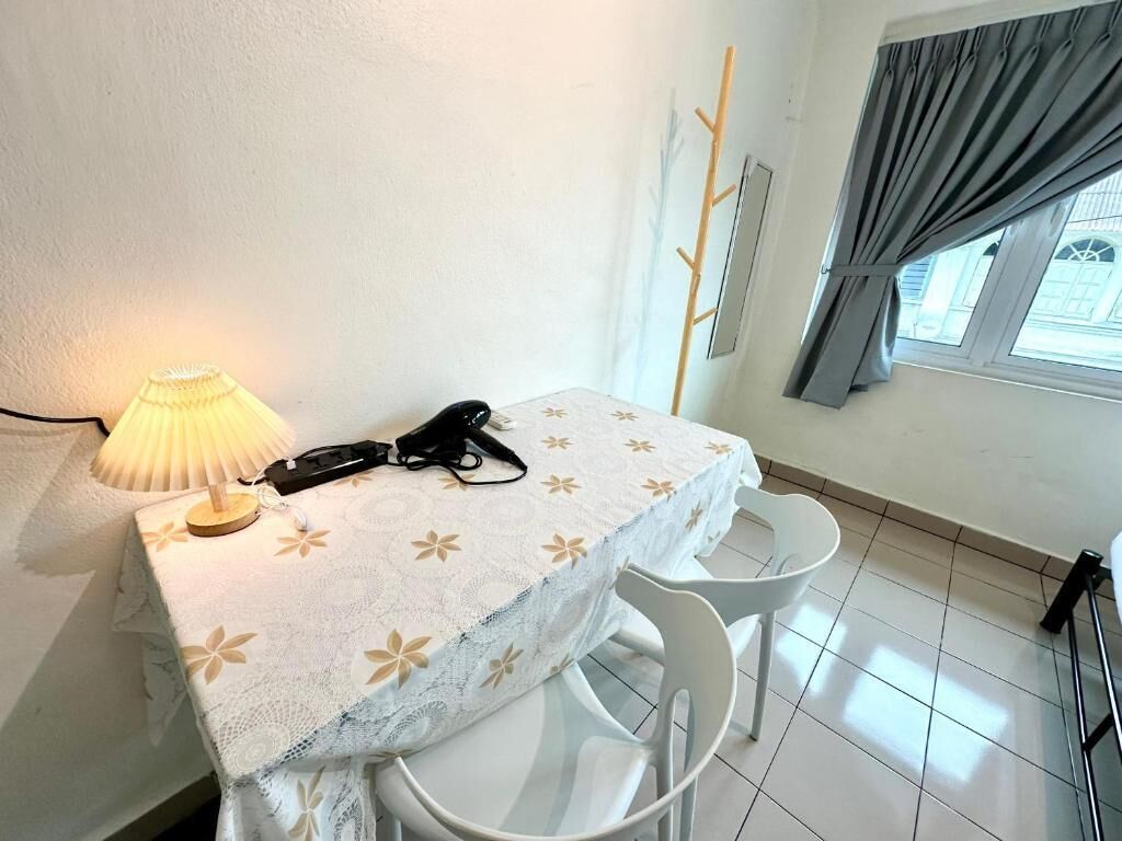 A small room with a table covered by a floral tablecloth, a lamp, a phone, and two white chairs.