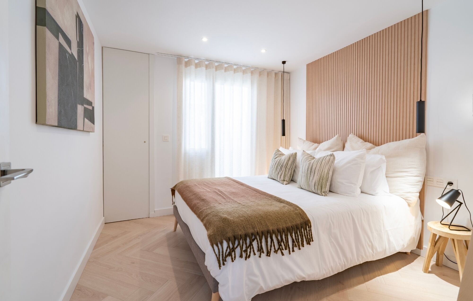 Een moderne slaapkamer met een groot bed, een houten hoofdbord, een nachtkastje met een lamp en een schilderij aan de muur.