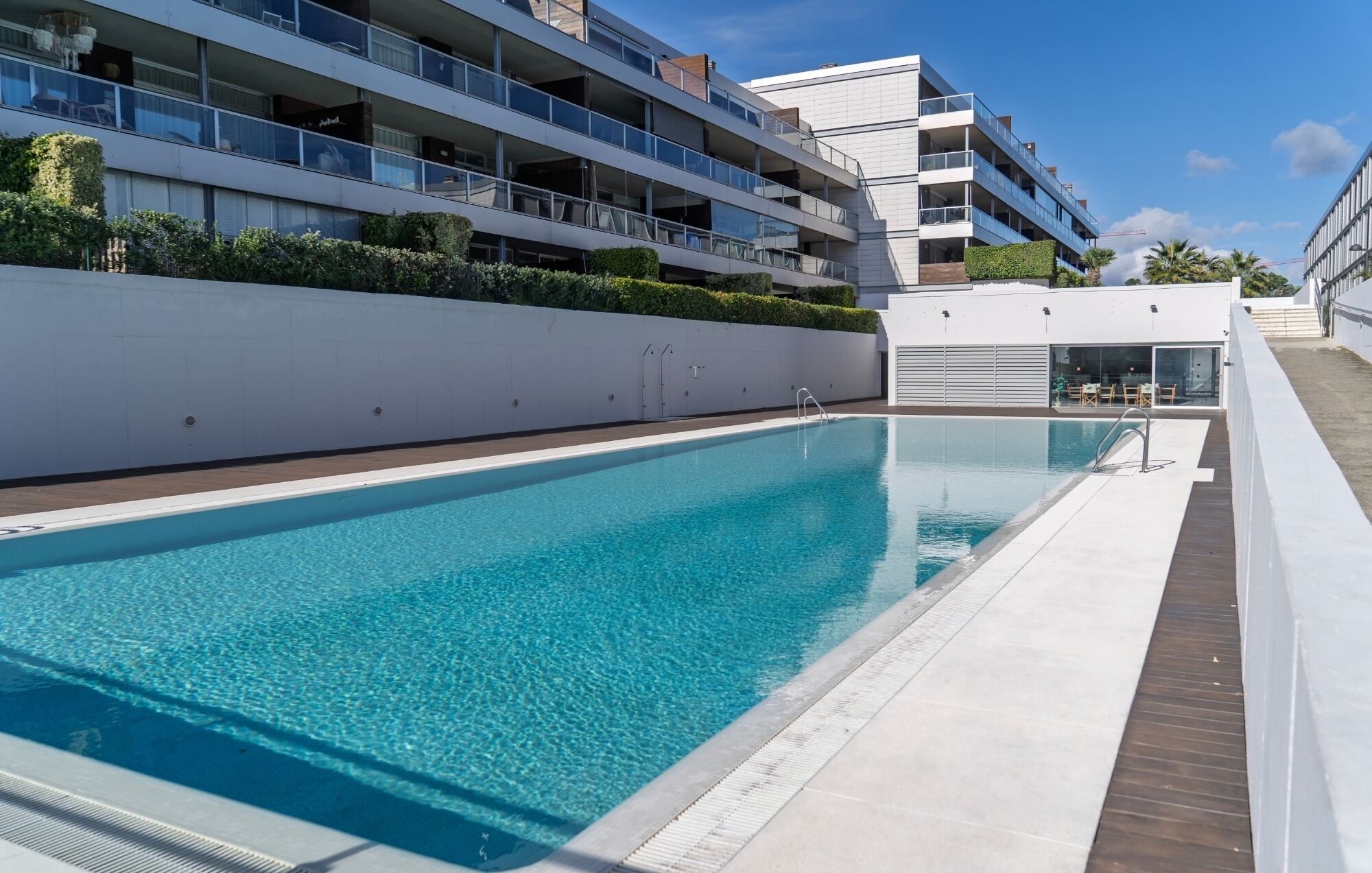 A modern residential building with a swimming pool, balconies, and a clear sky.