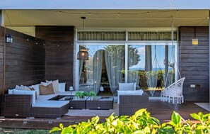 Un espace de vie extérieur moderne, aménagé avec des meubles en osier, un fauteuil suspendu et une porte vitrée donnant sur un paysage extérieur.