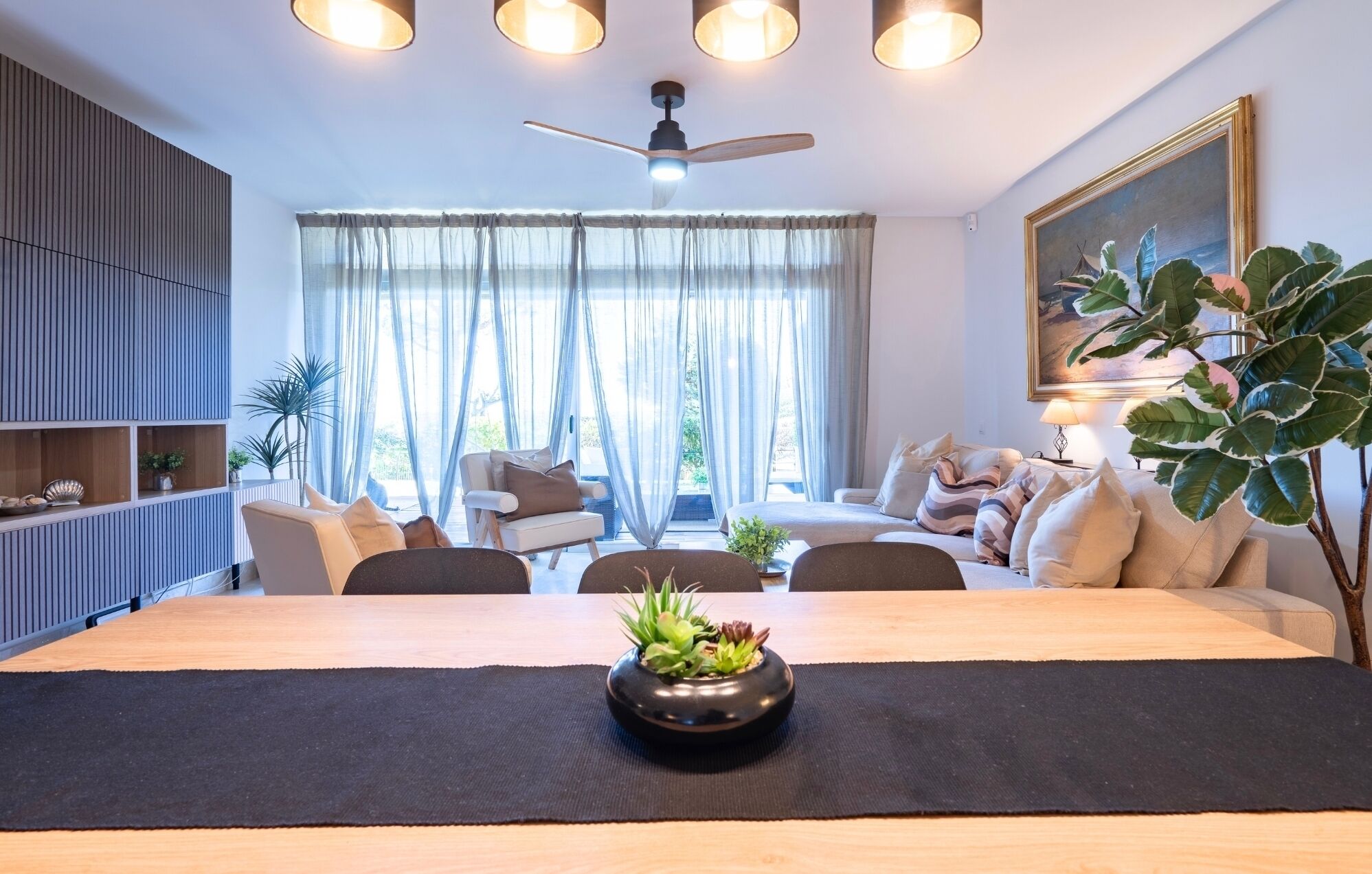 Een moderne woonkamer met een eettafel, banken en een plafondventilator.