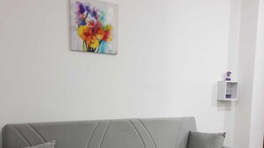 Un divano grigio con due cuscini, un tavolino da caffè in vetro e un quadro astratto colorato sulla parete.