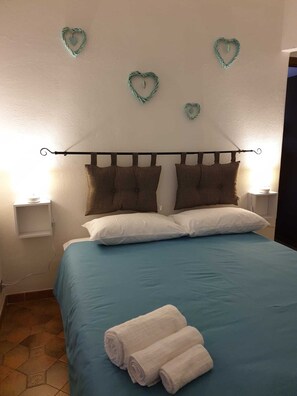 Ein Schlafzimmer mit Bett, Kissen, einem Kopfteil, herzförmigen Wanddekorationen und einem Nachttisch mit Lampe.