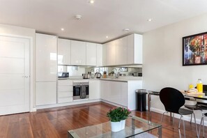 Une cuisine moderne avec des meubles blancs, un coin repas doté d’une table en verre et d’une chaise noire.