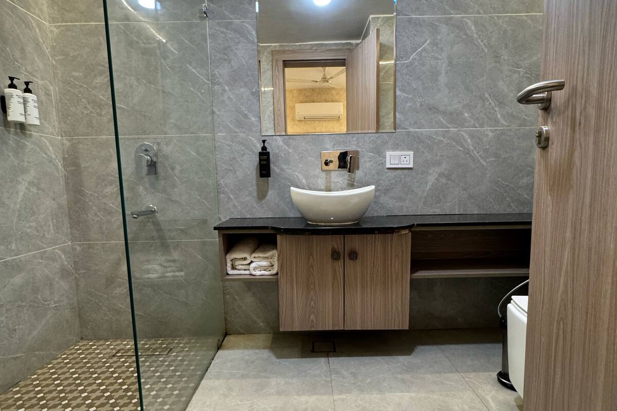 Une salle de bain moderne avec une douche à parois de verre, un sol carrelé en marbre, un meuble-lavabo en bois avec un vasque et un miroir au-dessus du lavabo.