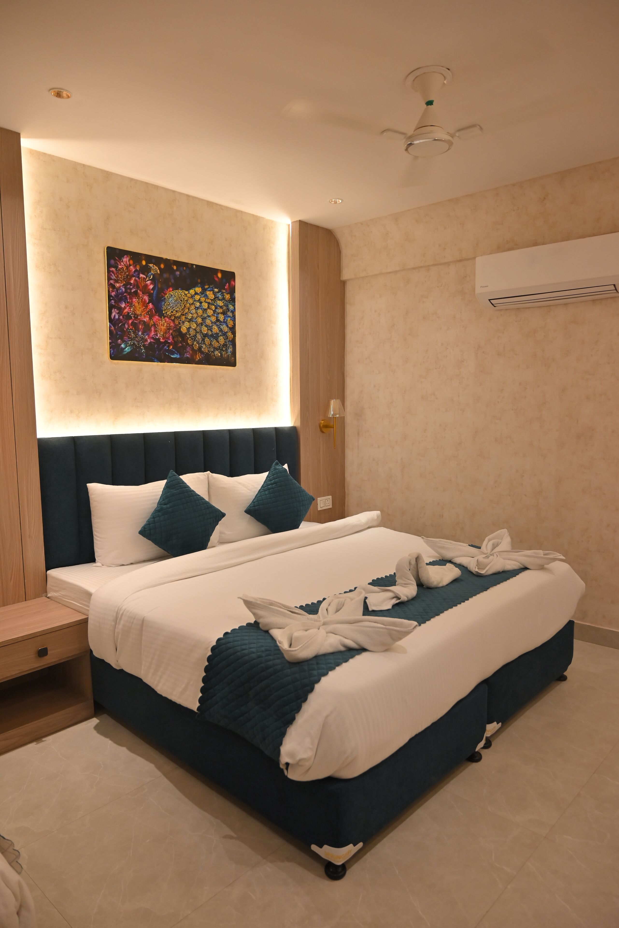 A modern hotel room with a large bed, a headboard with built-in lighting, a ceiling fan, and a wall-mounted air conditioner.