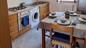 Une cuisine compacte avec des meubles en bois, une cuisinière à gaz, un lave-linge et une table à manger pour quatre personnes.