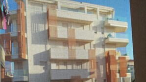 Une vue à travers une fenêtre munie d’un moustiquaire, qui révèle un immeuble à étages et doté de balcons.