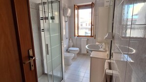Une salle de bain moderne dotée d’une douche à parois de verre, de toilettes, d’un lavabo et d’une fenêtre laissant entrer la lumière naturelle.