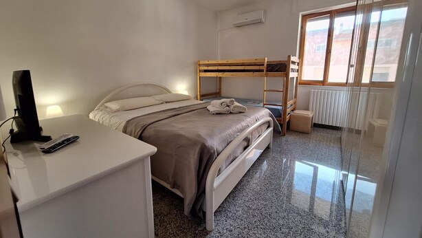 Une chambre avec un lit superposé, un bureau avec un ordinateur et une télécommande, un radiateur et une fenêtre donnant sur un paysage agréable.