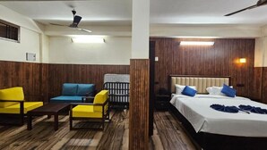 A hotel room with a bed, a sofa, a chair, and a small table. There is a ceiling fan and a wall-mounted light. - The Vintage Haven Munnar (Udumbanchola)