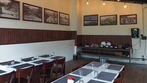 A restaurant with wooden paneling, tables with black and white placemats, and vintage photographs on the walls. - The Vintage Haven Munnar (Udumbanchola)