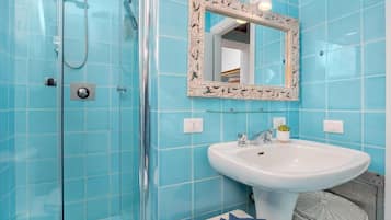A bathroom with a glass shower enclosure, a white sink, and a mirror with an ornate frame.