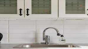 Una cocina con armarios blancos, un lavamanos de acero inoxidable y un grifo.