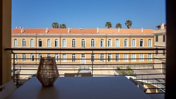 Un balcone con vista su un edificio con numerose finestre e cielo azzurro.