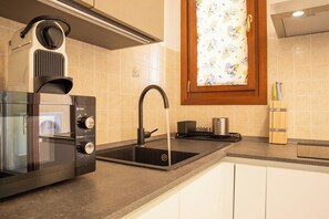 A kitchen with a built-in espresso machine, a sink, and a window with a floral curtain. - SPh24 apartment via Mazzini (Alghero)
