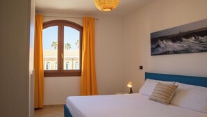 Una camera da letto con un letto, un comodino, una lampada, un quadro raffigurante delle onde e una finestra con tende.