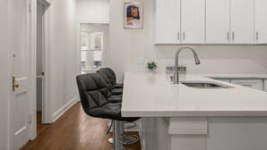 Una cocina moderna con armarios blancos, una barra con taburetes negros y un ventanal con vistas.