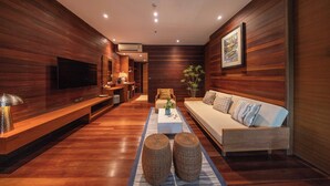 A modern living room with wooden paneling, a flat-screen TV, a sofa, a coffee table, and a plant. - Baan Krai Nao The Riverfront (Phra Pradaeng)