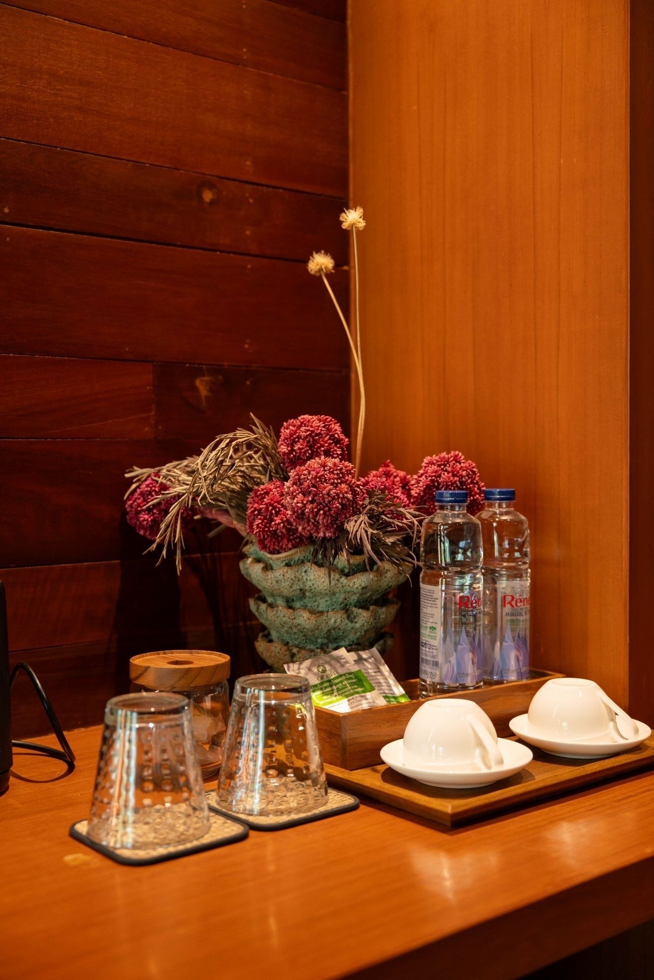 A wooden table with a vase of flowers, two water bottles, a wooden bowl, and two white bowls with spoons.