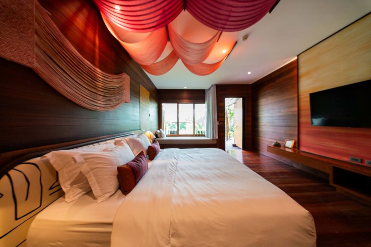 Een moderne hotelkamer met een groot bed, een flatscreen televisie aan de muur en uitzicht op het omliggende landschap door een groot raam.