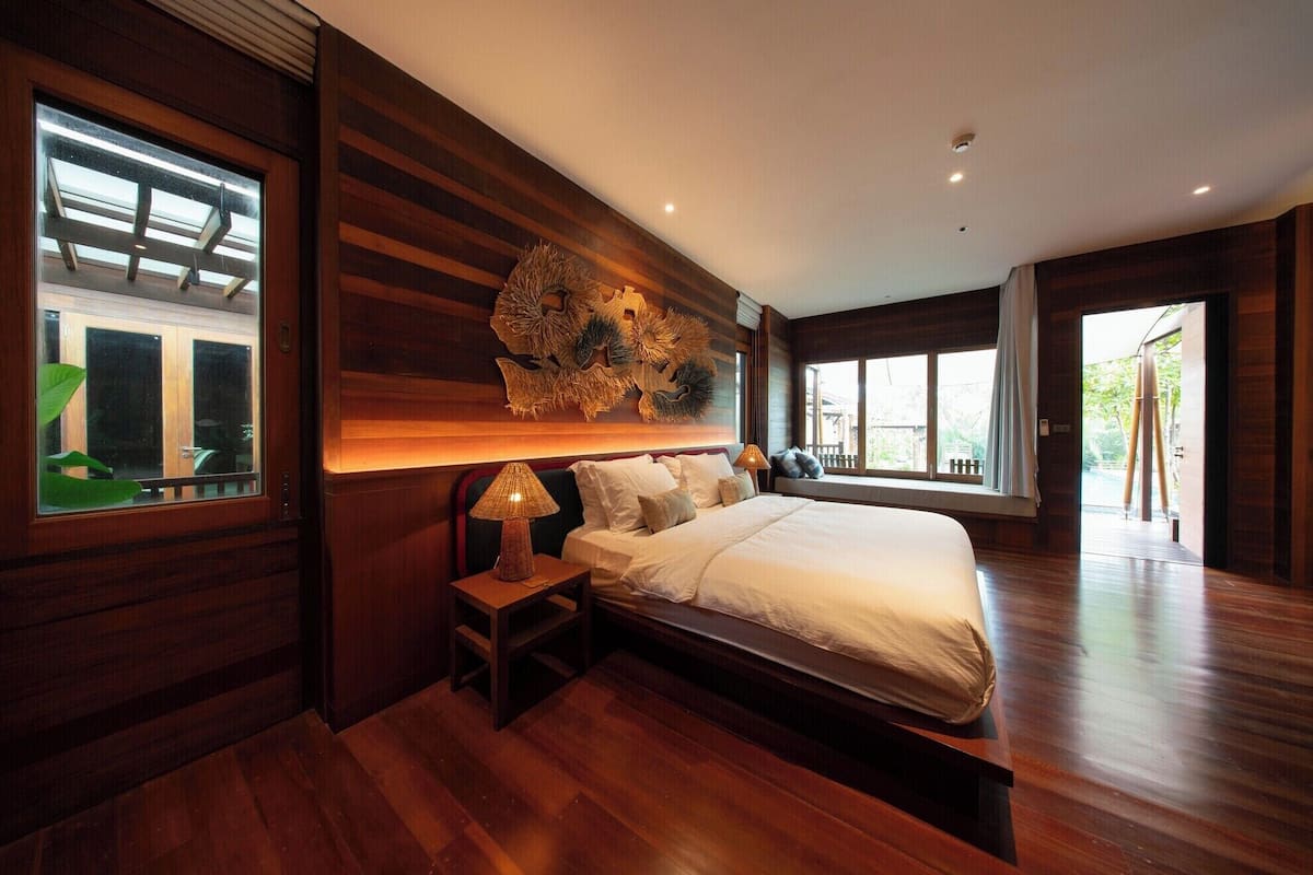 Een moderne slaapkamer met een groot bed, houten lambrisering, een decoratief kunstwerk en grote ramen.