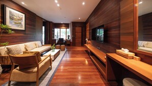 A modern living room with a wooden floor, a sofa set, a TV, and a large window. - Baan Krai Nao The Riverfront (Phra Pradaeng)