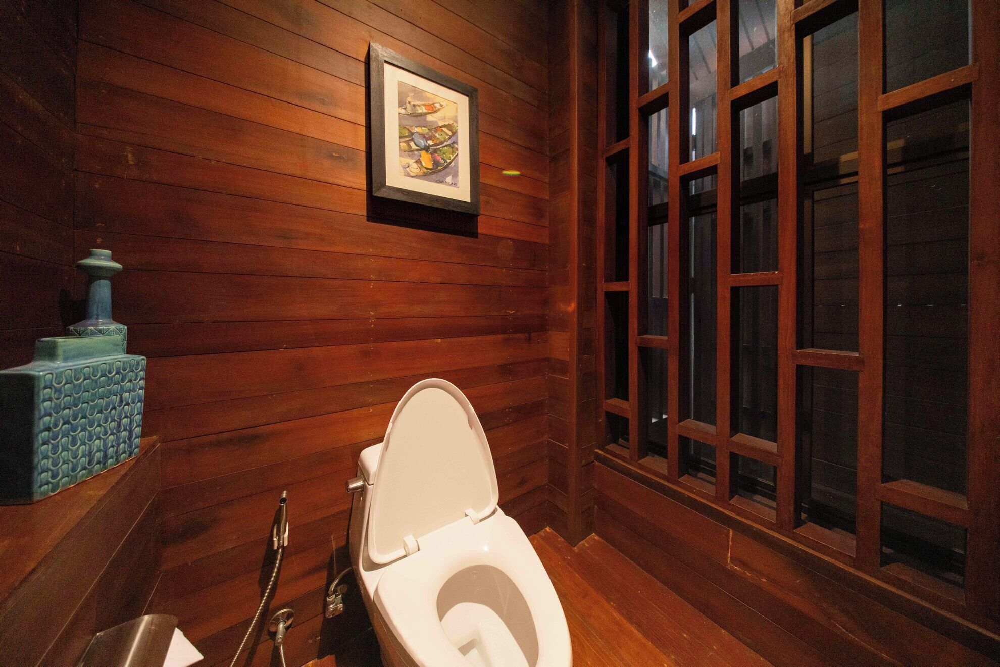 A wooden bathroom with a toilet, a sink, and a window.