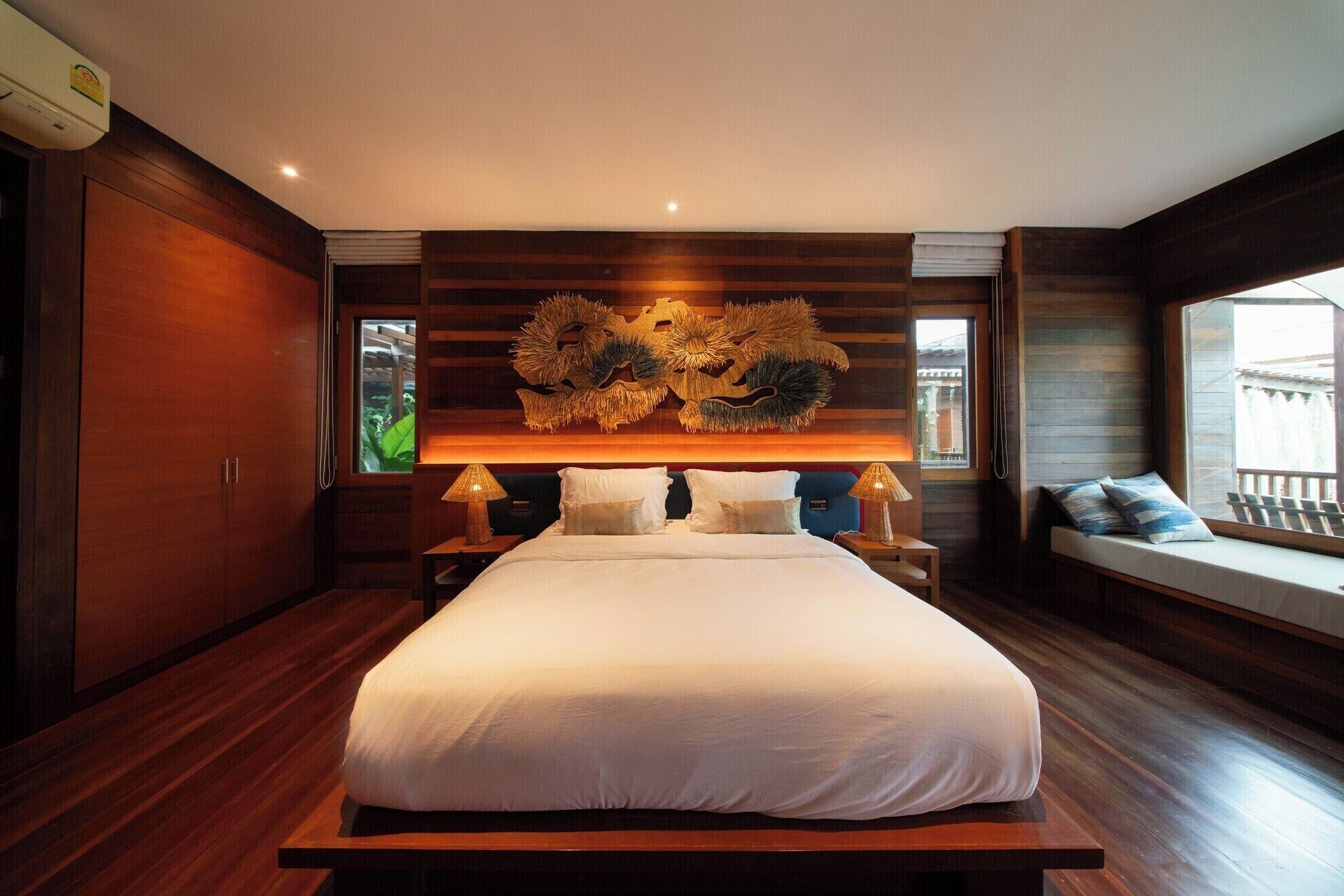 A spacious bedroom with a large bed, wooden paneling, a decorative wall piece, and a window with a view.