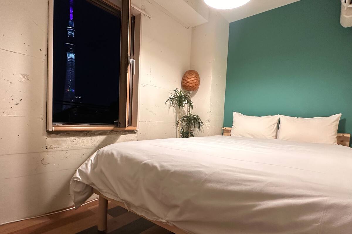 Ein Schlafzimmer mit einem Bett, einem Fenster mit Blick auf einen Turm, einer Pflanze und einer turquoise farbenen Akzentwand.