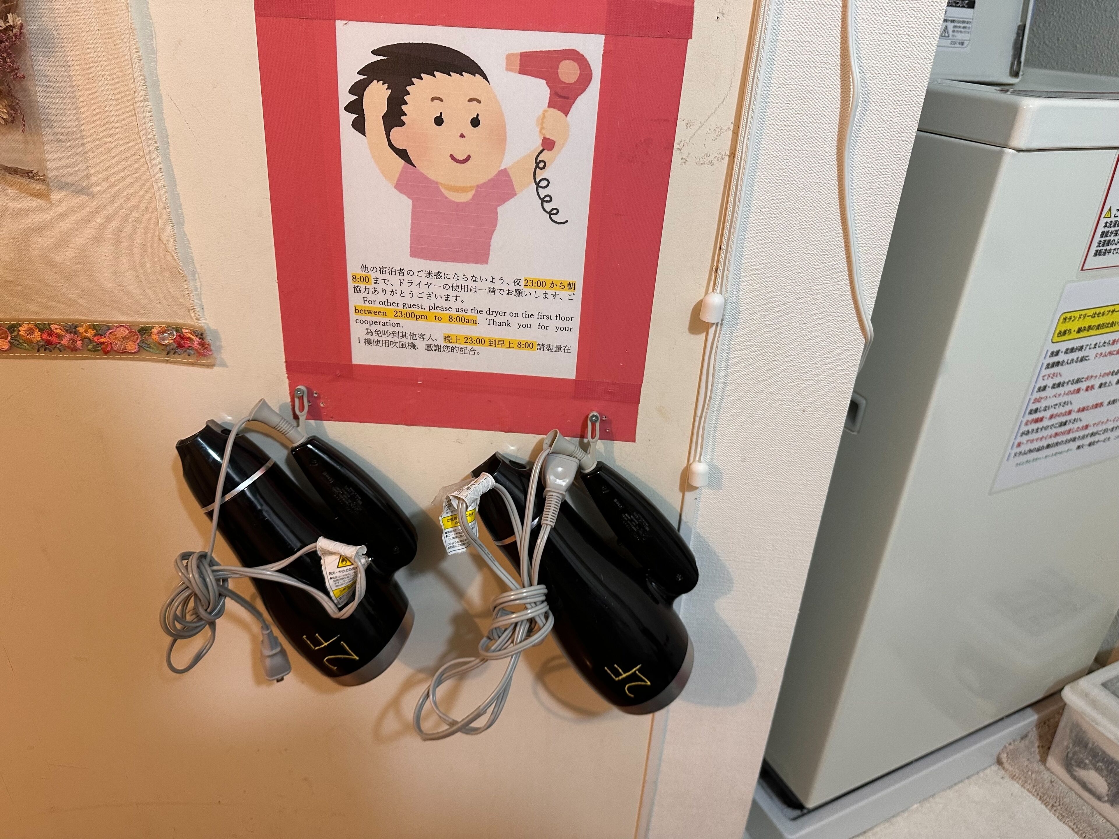 A notice board with a cartoon character holding a hairdryer, and two black charging cases with cords hanging below.