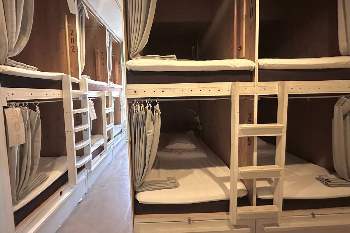 Ein Schlafsaalzimmer mit Etagenbetten, Vorhängen, einer Leiter und nummerierten Ablagefächern.