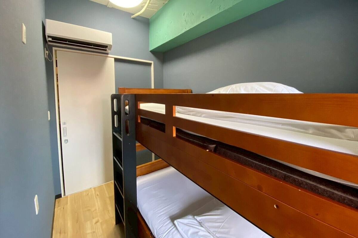 Ein Schlafraum mit Etagenbett, einem Holzkopfstück, einer weißen Matratze und einer Deckenleuchte.