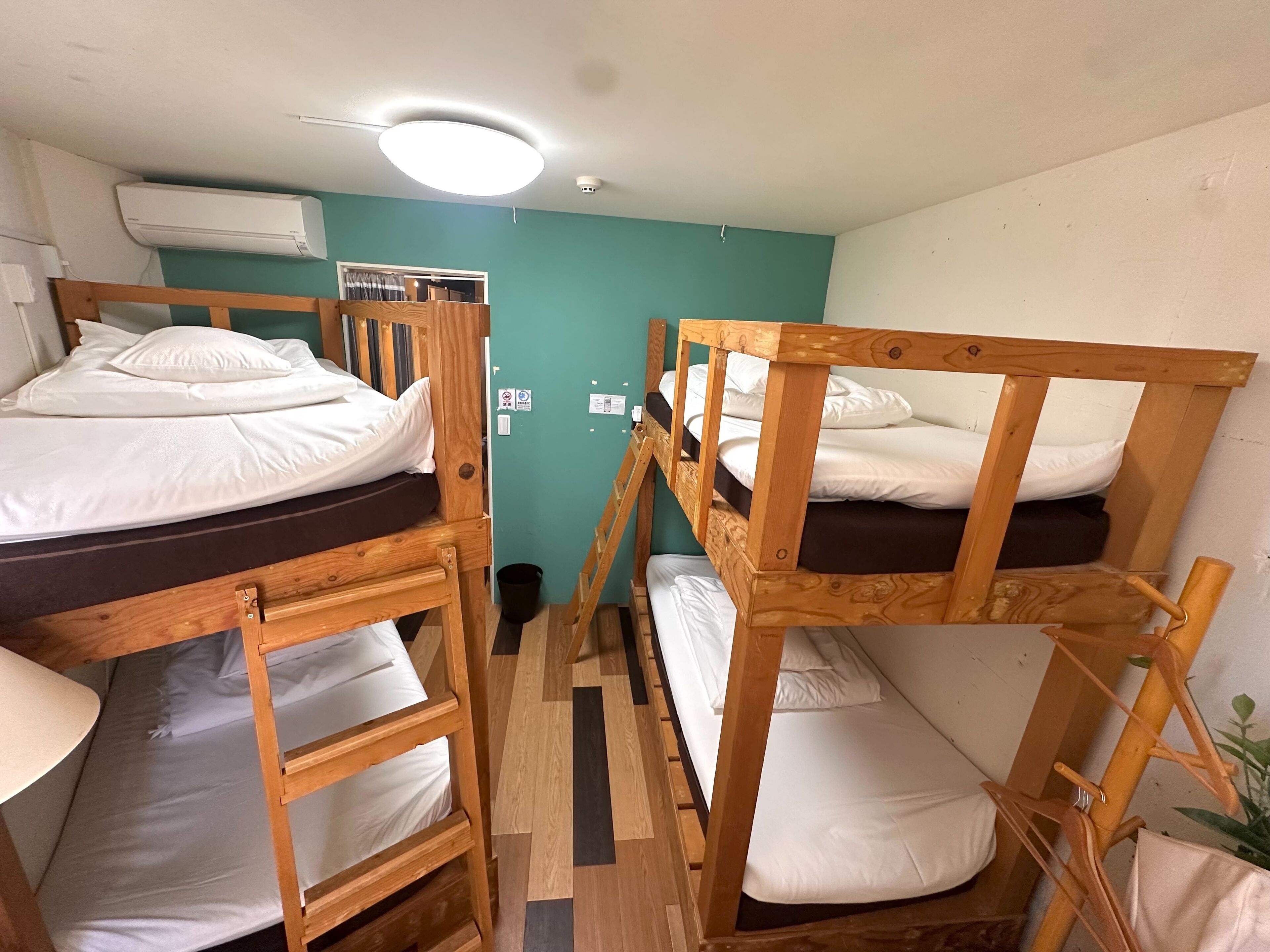 Une chambre de dortoir équipée de lits superposés, d’un ventilateur de plafond, d’un appareil de climatisation et d’une petite poubelle.