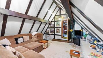 Een knus zolderkamertje met een bruine bank, een klein houten tafeltje en een televisie.