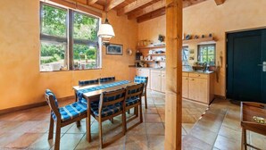 A dining area with a wooden table and chairs, a window with a view of greenery, and a kitchen area with cabinets and a sink. - Kitchen-living room with bathroom in a historic barn (Hennef)