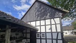 A traditional half-timbered building with a stone-paved courtyard, wooden benches, and a hanging light fixture. - Kitchen-living room with bathroom in a historic barn (Hennef)
