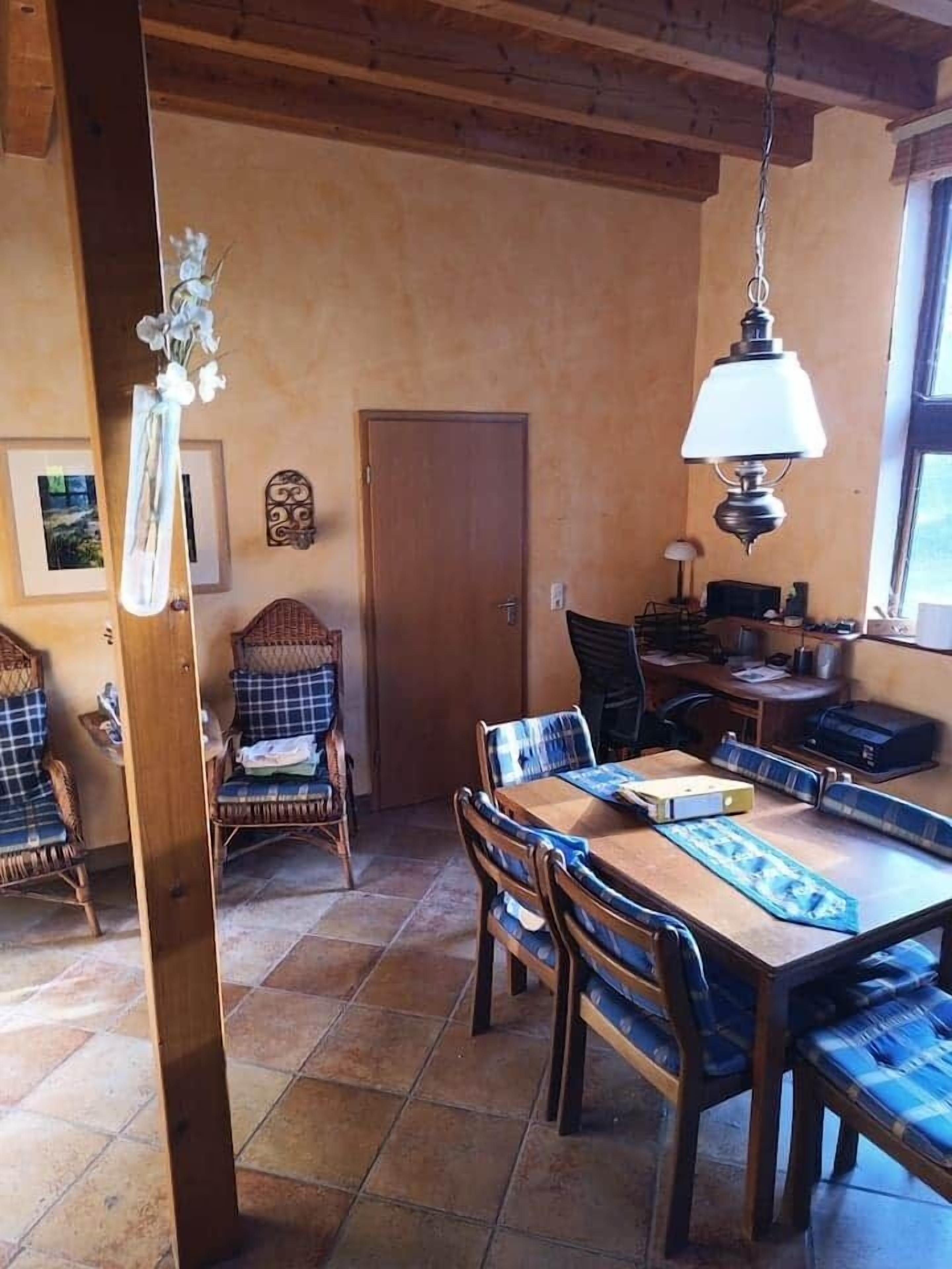 A dining area with a wooden table and chairs, a hanging light fixture, and a door in the background.